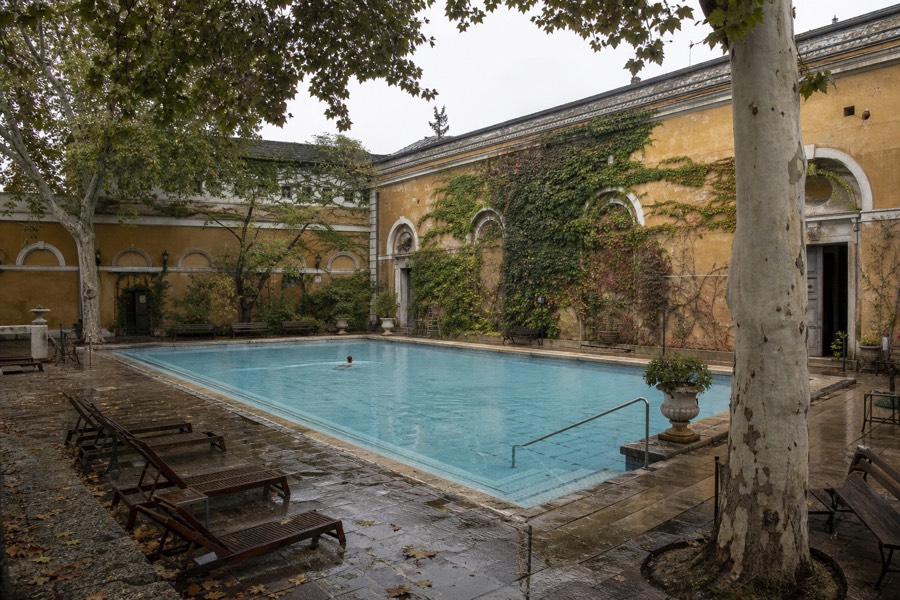 Quiet morning at a leafy old Budapest bath courtyard with a still outdoor pool used by local swimmers