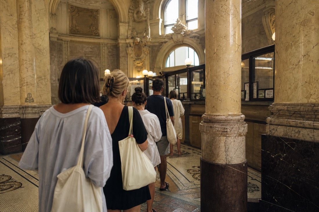 Blurred queue of visitors seen from behind at an ornate ticket hall inside a historic Budapest bathhouse