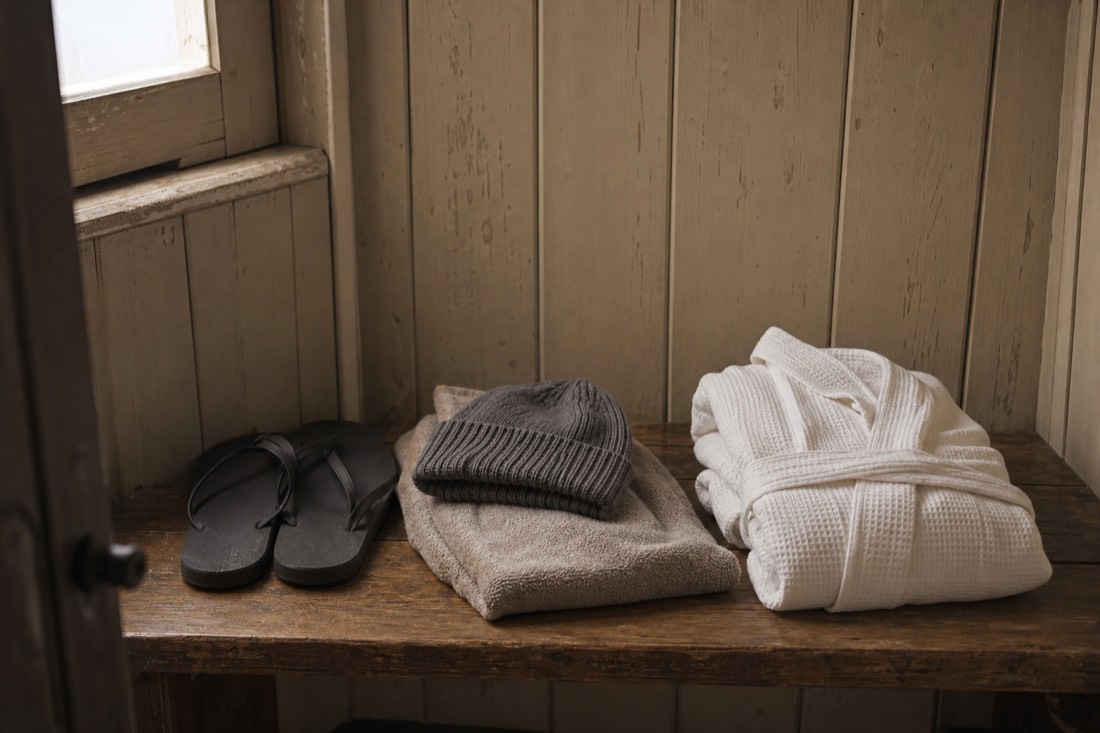Winter bath essentials laid out on a wooden changing-cabin bench, flip-flops, wool hat, towel and a folded robe