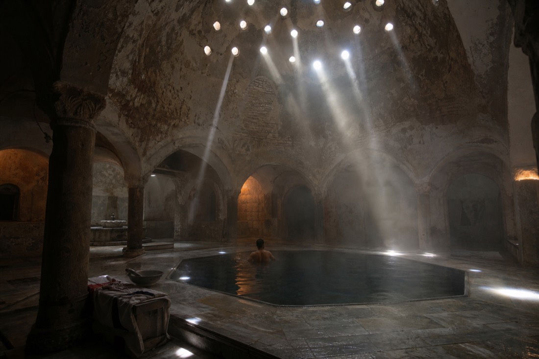 Sunbeams falling through a domed Ottoman bath ceiling onto an octagonal thermal pool