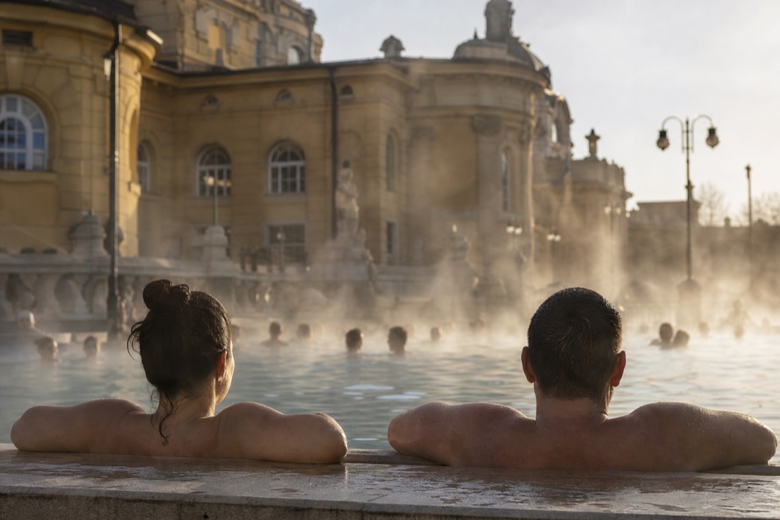 Bathers relaxing in a steaming outdoor thermal pool beside century-old bath architecture in Budapest