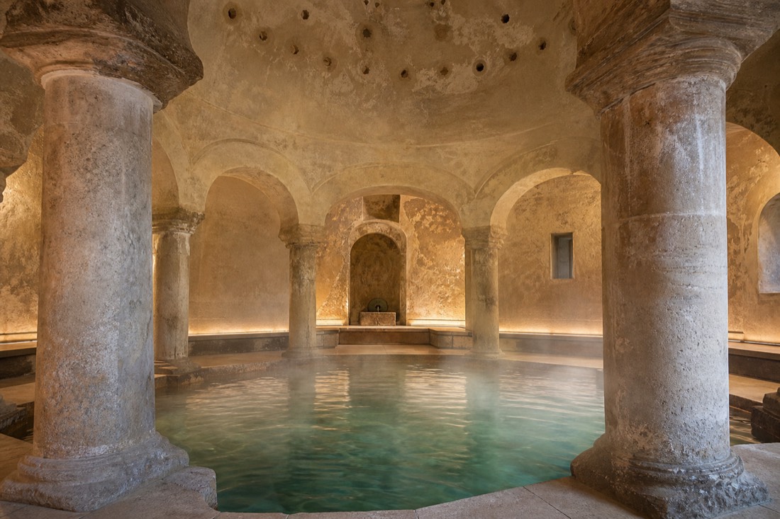 Steam drifting past stone columns and a small warm pool inside a restored Ottoman bath on the Buda side