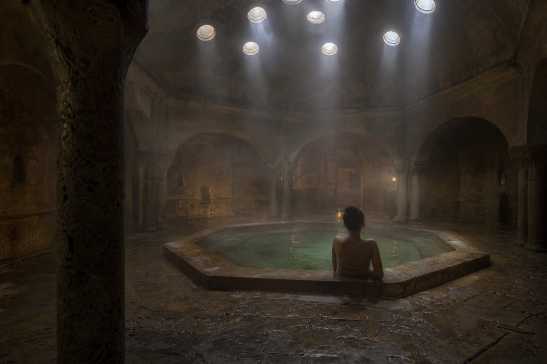 Dim octagonal Ottoman bath dome with shafts of light falling on still thermal water in Budapest