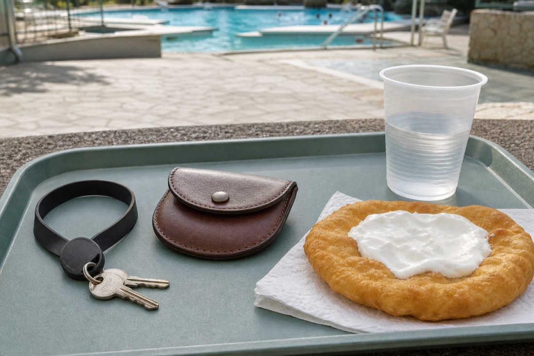 Locker key wristband and a small coin purse resting on a cafe tray beside a fried flatbread at a bath snack bar