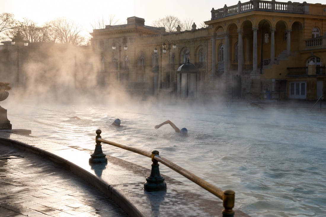 Early morning lap swimmers in an outdoor pool at a Budapest thermal bath with steam rising off the water