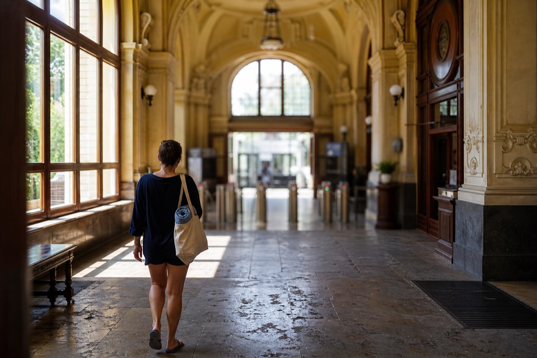 Entrance hall of a historic Budapest bath with morning light and a visitor carrying a towel bag