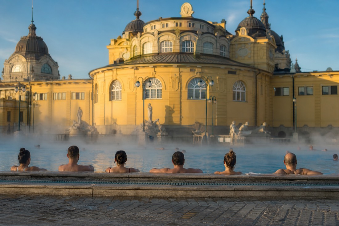 Bathers relaxing at the edge of a steaming outdoor thermal pool in Budapest
