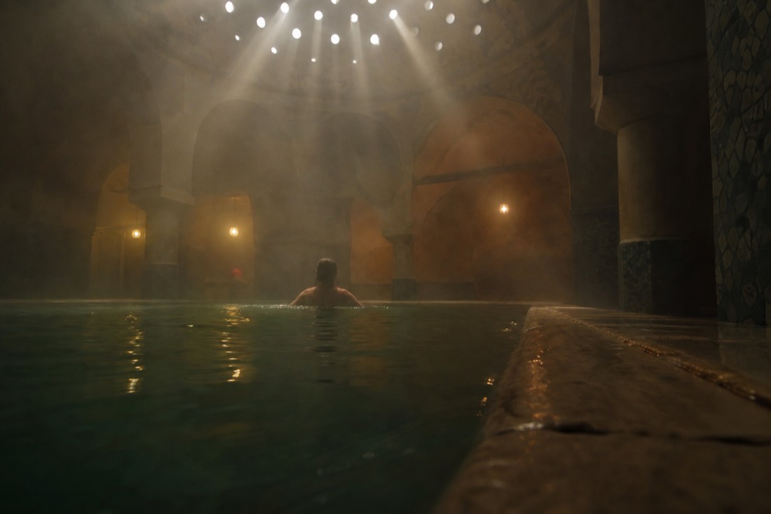 Bather resting at the edge of a warm octagon-lit thermal pool in an Ottoman bath section in Budapest