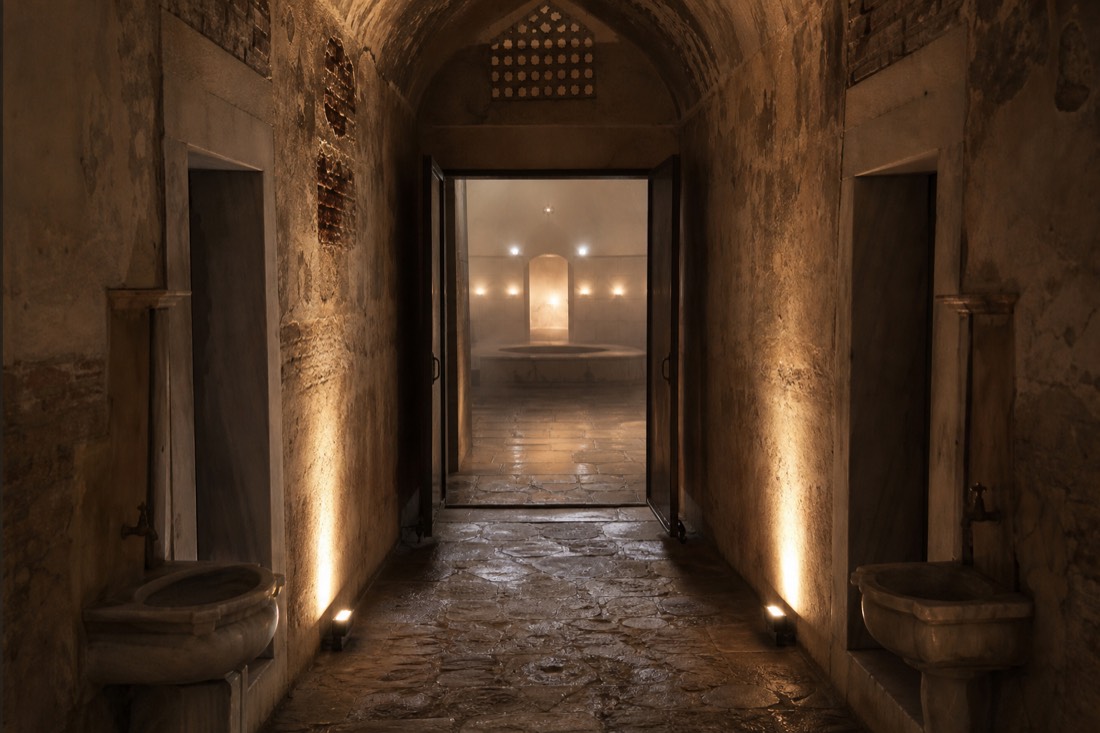 Quiet arched stone corridor leading toward a warm bathing hall in a restored Ottoman bath