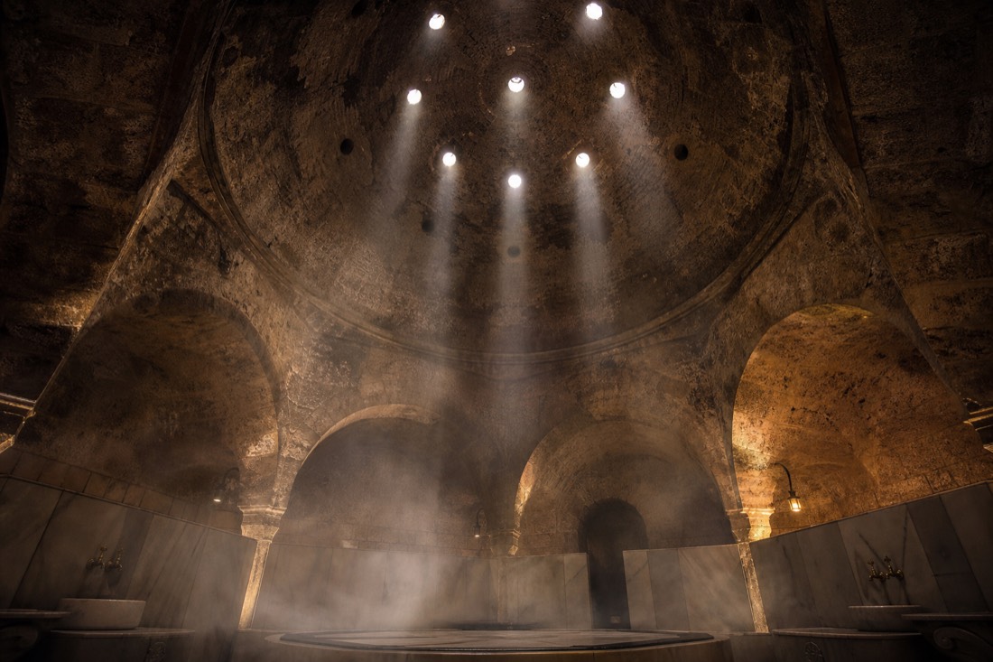 Stone cupola and dim warm light inside a historic Ottoman Turkish bath hall in Buda