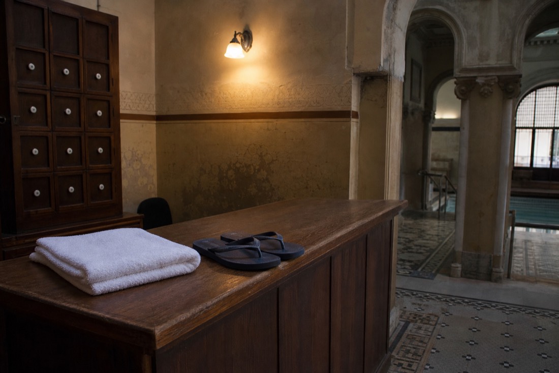 Simple wooden reception counter inside a historic Buda bath house, with a folded towel and flip-flops laid out beside it