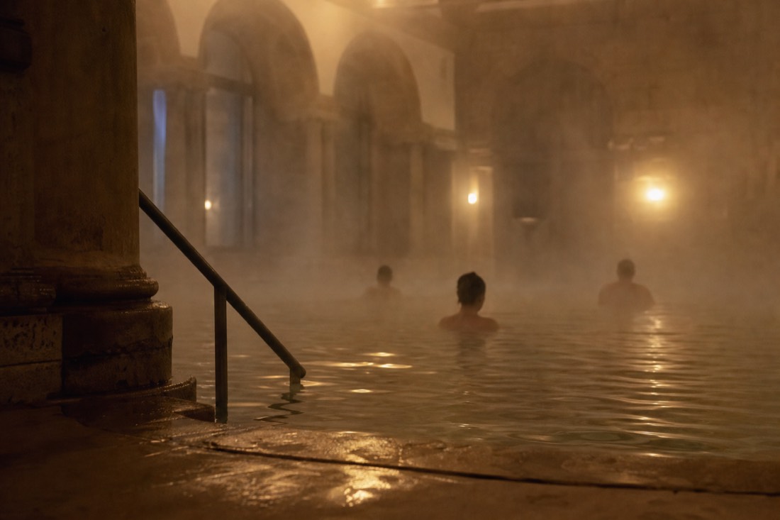 Calm thermal pool with a few bathers' silhouettes in soft steam inside a Budapest Turkish bath