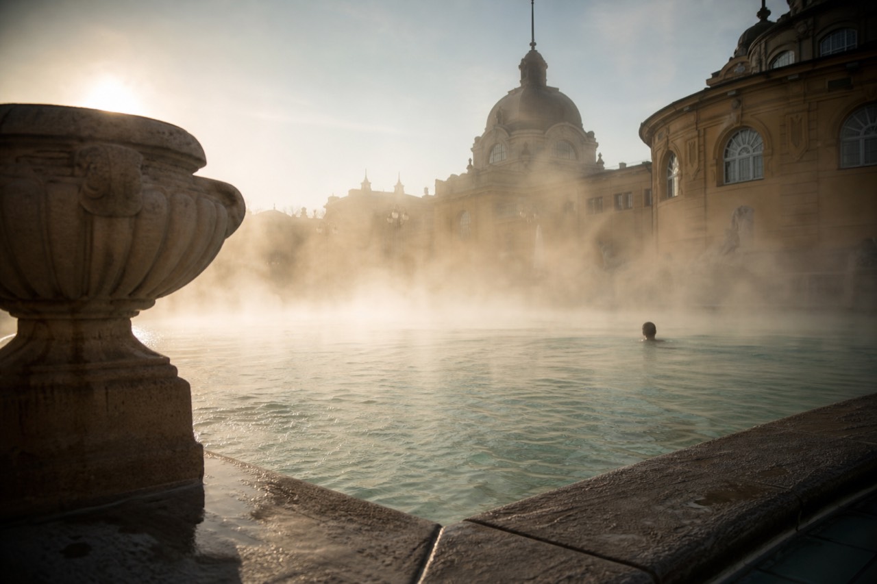 Early morning steam drifting over warm water at a nearly empty outdoor thermal bath in Budapest